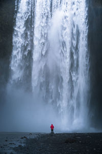 Rear view of man standing by skogafoss waterfall 