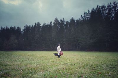 Man with dog standing on field against trees