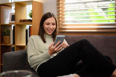 Young woman using mobile phone while sitting at home