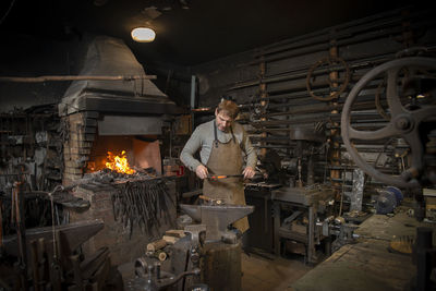 The blacksmith manually forging the red-hot metal on the anvil in smithy with spark fireworks