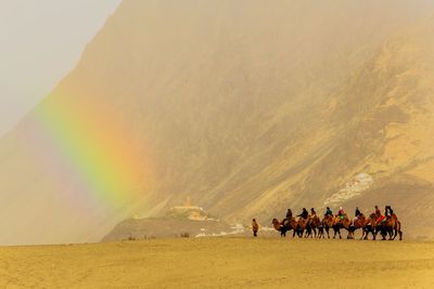 People riding animals on sand against mountains