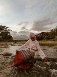 Young woman wearing traditional clothing sitting on rock amidst river