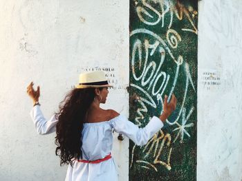Rear view of young woman standing in front of graffiti wall