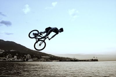 Man riding bicycle by sea against sky