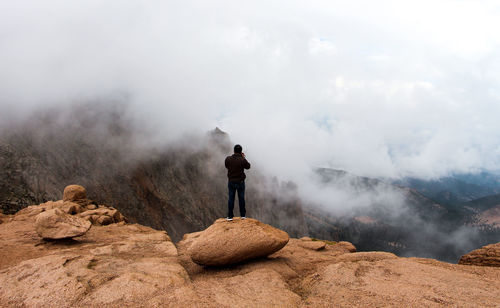 Rear view of man photographing mountain landscape against cloudy sky