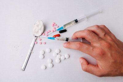 Cropped hand holding syringe with pills on table