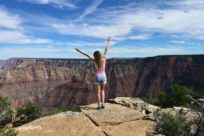 Rear view of woman standing on cliff against sky