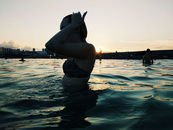 Woman standing by swimming pool against sky during sunset