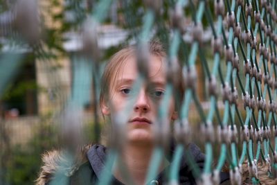 Portrait of serious girl seen through chainlink fence