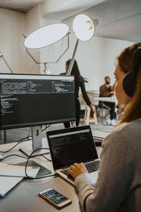 Young female hacker doing coding on computer in office