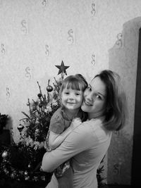 Portrait of smiling mother carrying daughter by christmas tree at home