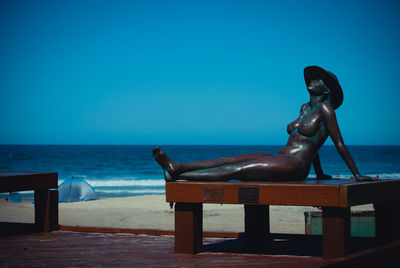 Statue on beach against clear blue sky