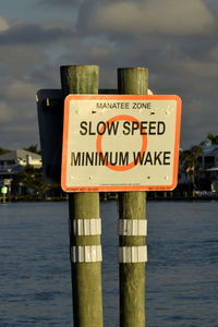 Information sign by sea against sky