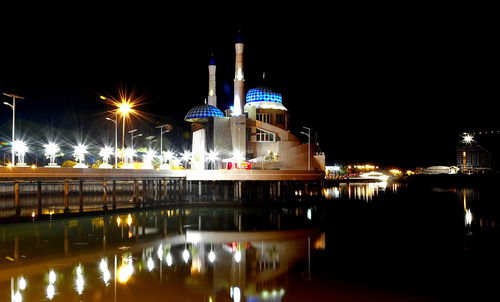 Illuminated buildings by river against sky at night