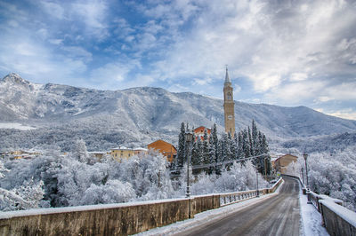 Road leading towards town against cloudy sky during winter