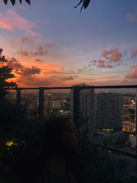 Woman by buildings against sky during sunset