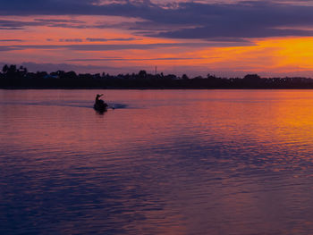 Silhouette person in sea against sky during sunset