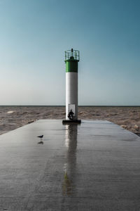 Lighthouse by sea against clear sky