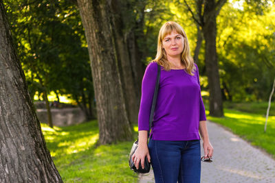 Young blonde woman standing in park. green nature background. mature blonde woman smiling 