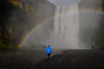 Scenic view of rainbow over waterfall against sky