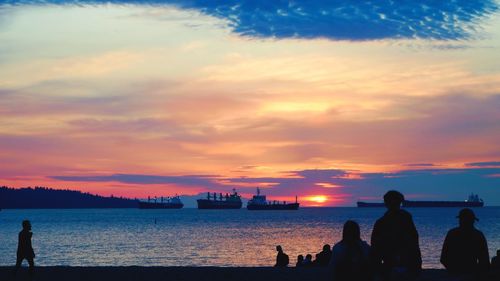 Silhouette people by sea against sky during sunset