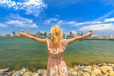 Woman with arms outstretched standing at beach against sky