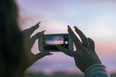 Man photographing with mobile phone against sky