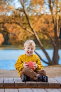 Portrait of cheerful boy sitting on table against lake