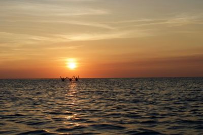 Silhouette man in sea against sky during sunset