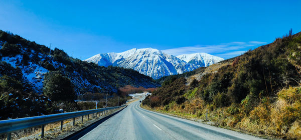 Road amidst snowcapped mountains against clear blue sky