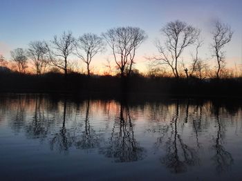 Reflection of bare trees in lake during sunset