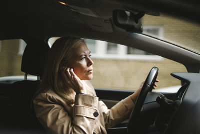 Businesswoman adjusting in-ear headphones while driving car