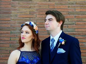 Portrait of young couple standing against brick wall