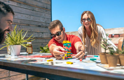Concentrated man catching jenga game piece next to colleagues on terrace