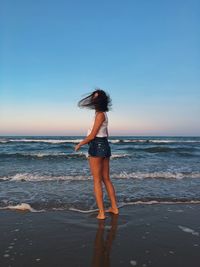 Full length of woman standing on shore at beach against clear sky