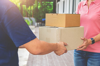 Midsection of delivery person giving boxes to woman outdoors