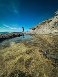 Rear view of woman standing on rock against sky