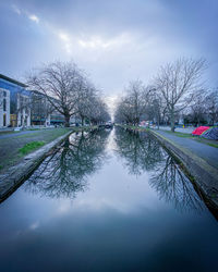 Canal amidst bare trees against sky in city
