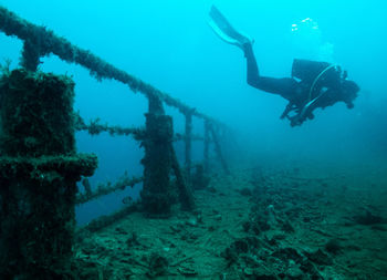 Scuba diver swimming by old railing in sea