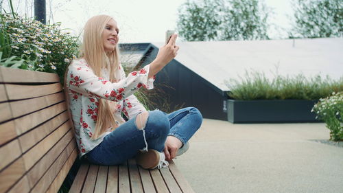 Woman taking selfie with mobile phone while sitting on bench