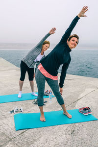 Mother and daughter exercising at beach against sky