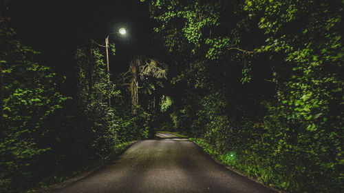Empty road amidst trees at night