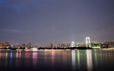 Illuminated city by river against sky at night