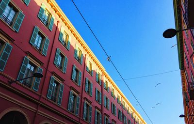 Low angle view of seagulls flying over building against clear blue sky