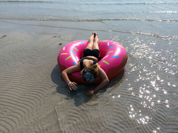 Rear view of woman lying down on inflatable ring at beach