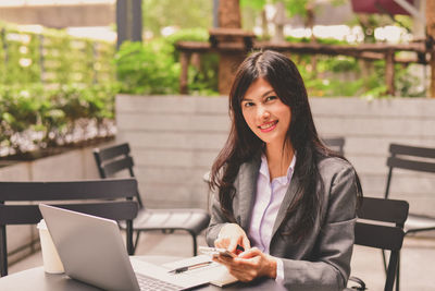 Portrait of young woman using phone while sitting on table