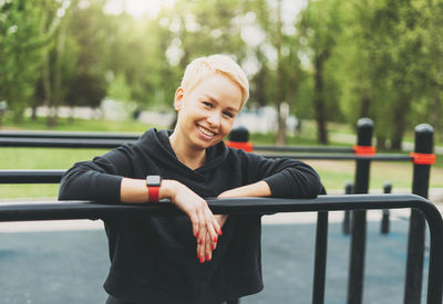 Portrait of smiling woman standing by railing in park