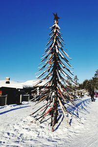 Dead tree on snow covered field against clear blue sky