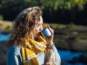 Young curly woman traveller drinking coffee from thermos