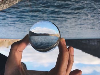 Cropped hand of person holding crystal ball at beach